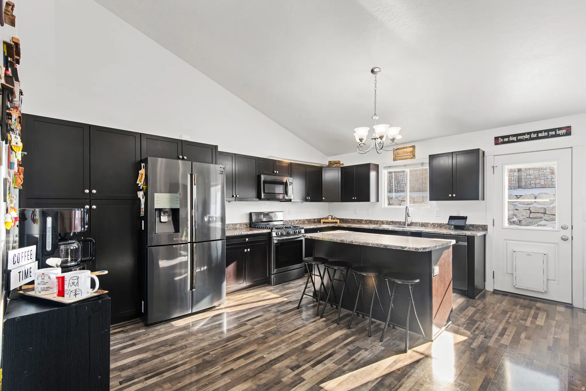 Kitchen with appliances with stainless steel finishes, a breakfast bar, pendant lighting, a kitchen island, and dark cabinets