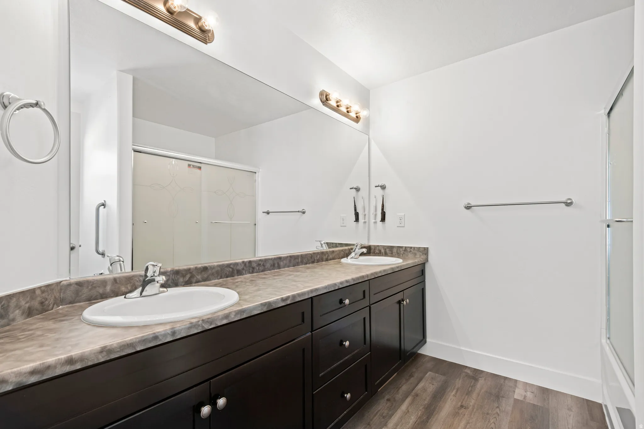 Bathroom with a shower with shower door, double vanity, and dark wood-style floors
