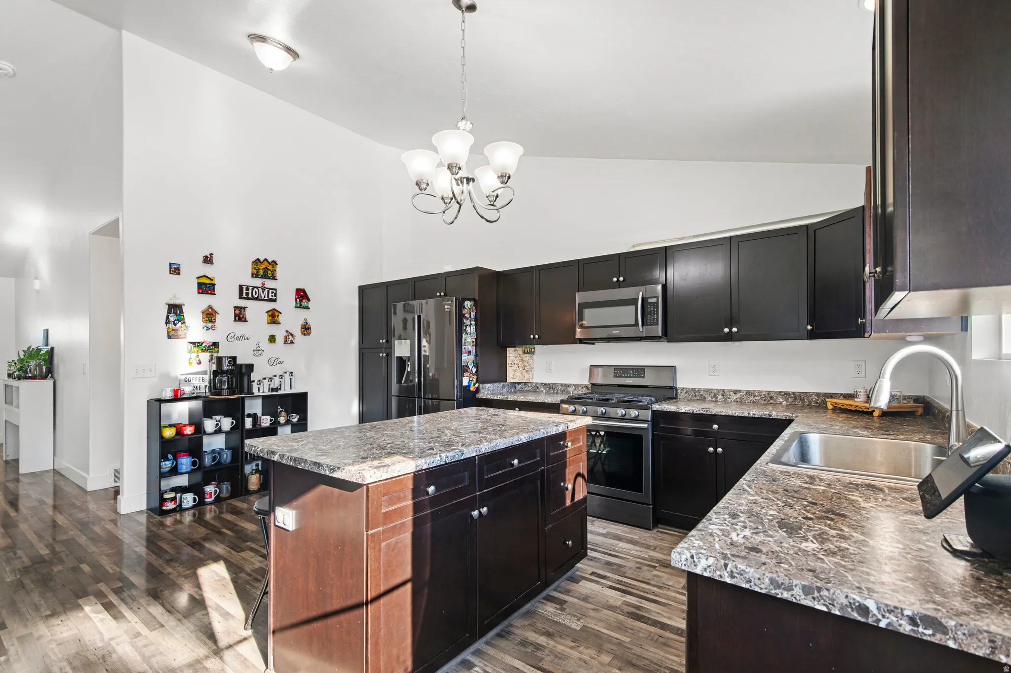 Kitchen with high vaulted ceiling, appliances with stainless steel finishes, dark wood finished floors, decorative light fixtures, and a kitchen island
