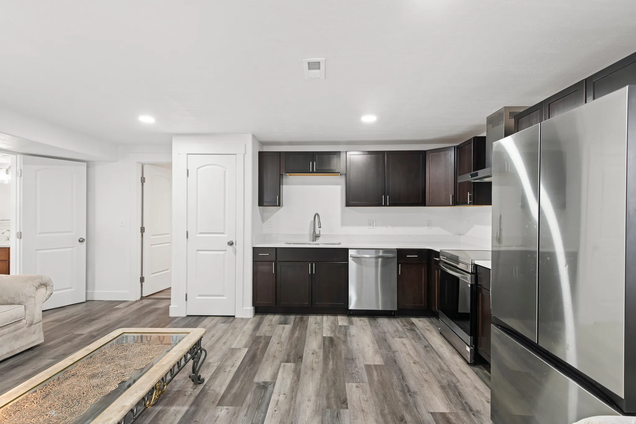 Kitchen with appliances with stainless steel finishes, dark brown cabinets, recessed lighting, light wood-style flooring, and wall chimney range hood