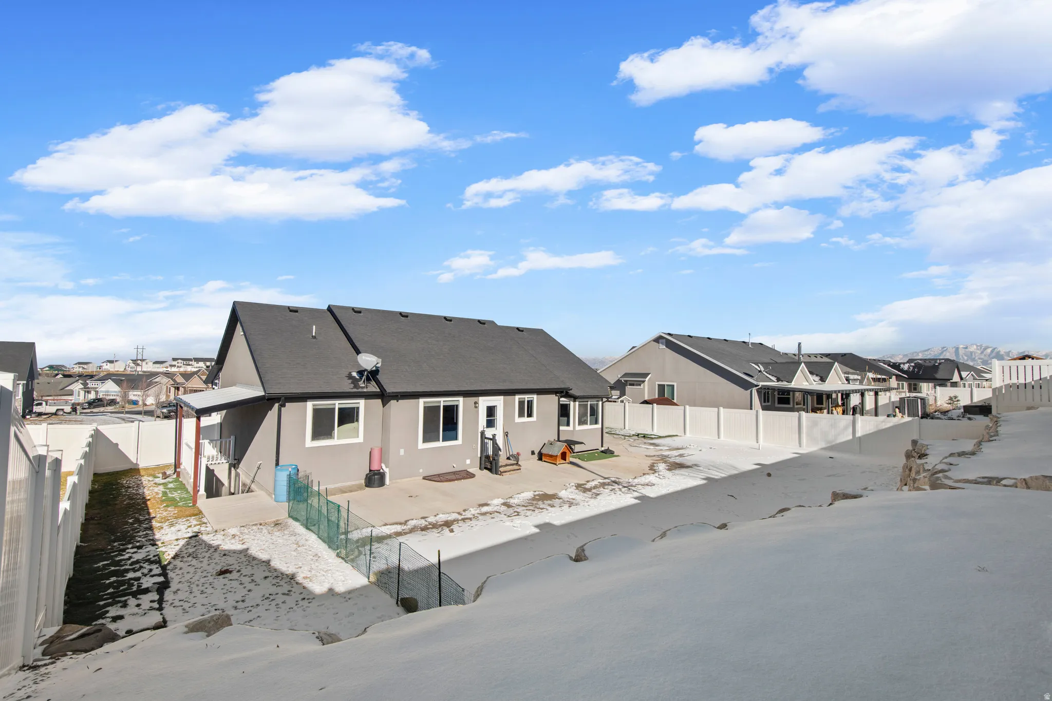 Snow covered back of property featuring a fenced backyard, a residential view, a patio, and stucco siding