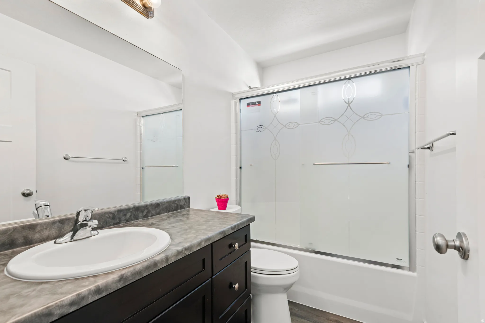Full bath featuring vanity, bath / shower combo with glass door, and dark wood-style flooring