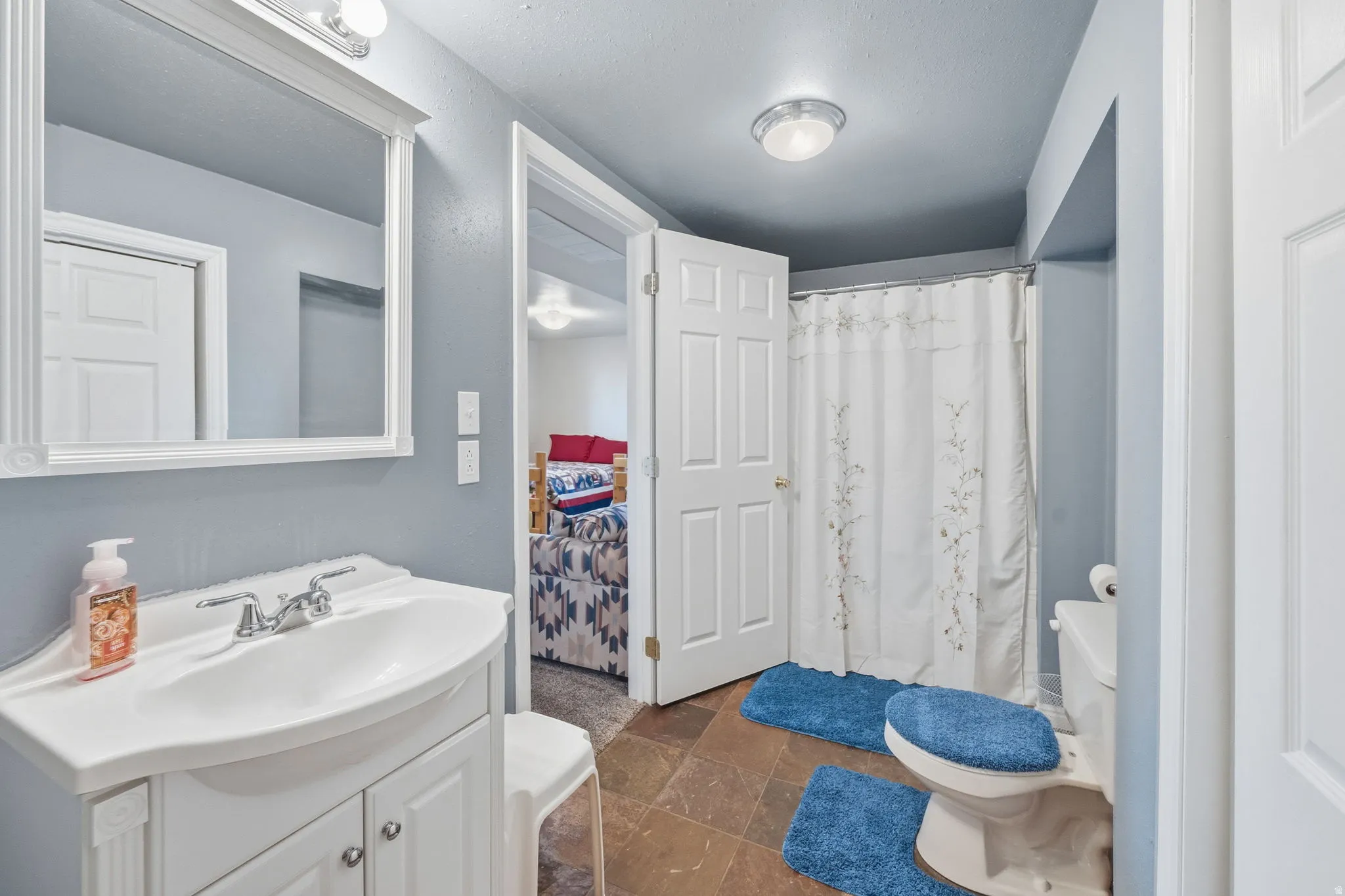 Bathroom with vanity, a shower with curtain, and stone tile flooring