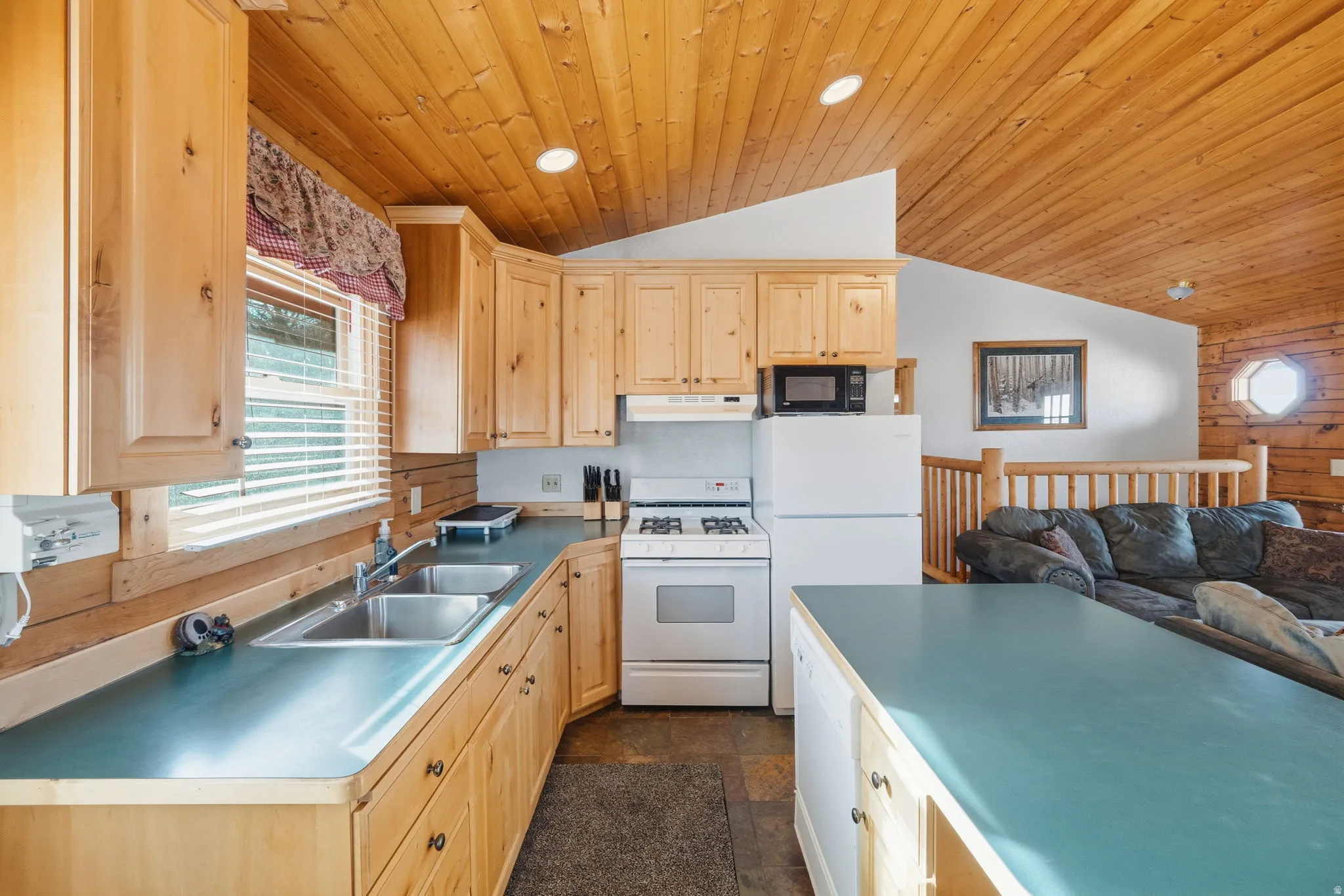 Kitchen with white appliances, light brown cabinetry, wooden walls, wooden ceiling, and lofted ceiling