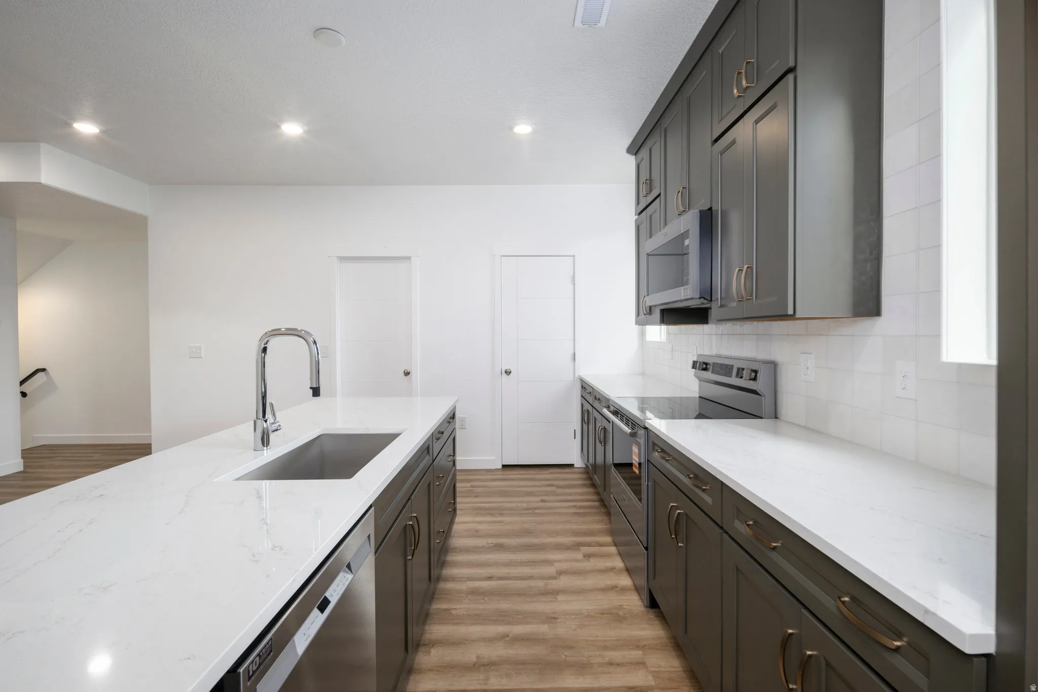 Kitchen featuring appliances with stainless steel finishes, light stone countertops, light wood-type flooring, backsplash, and recessed lighting
