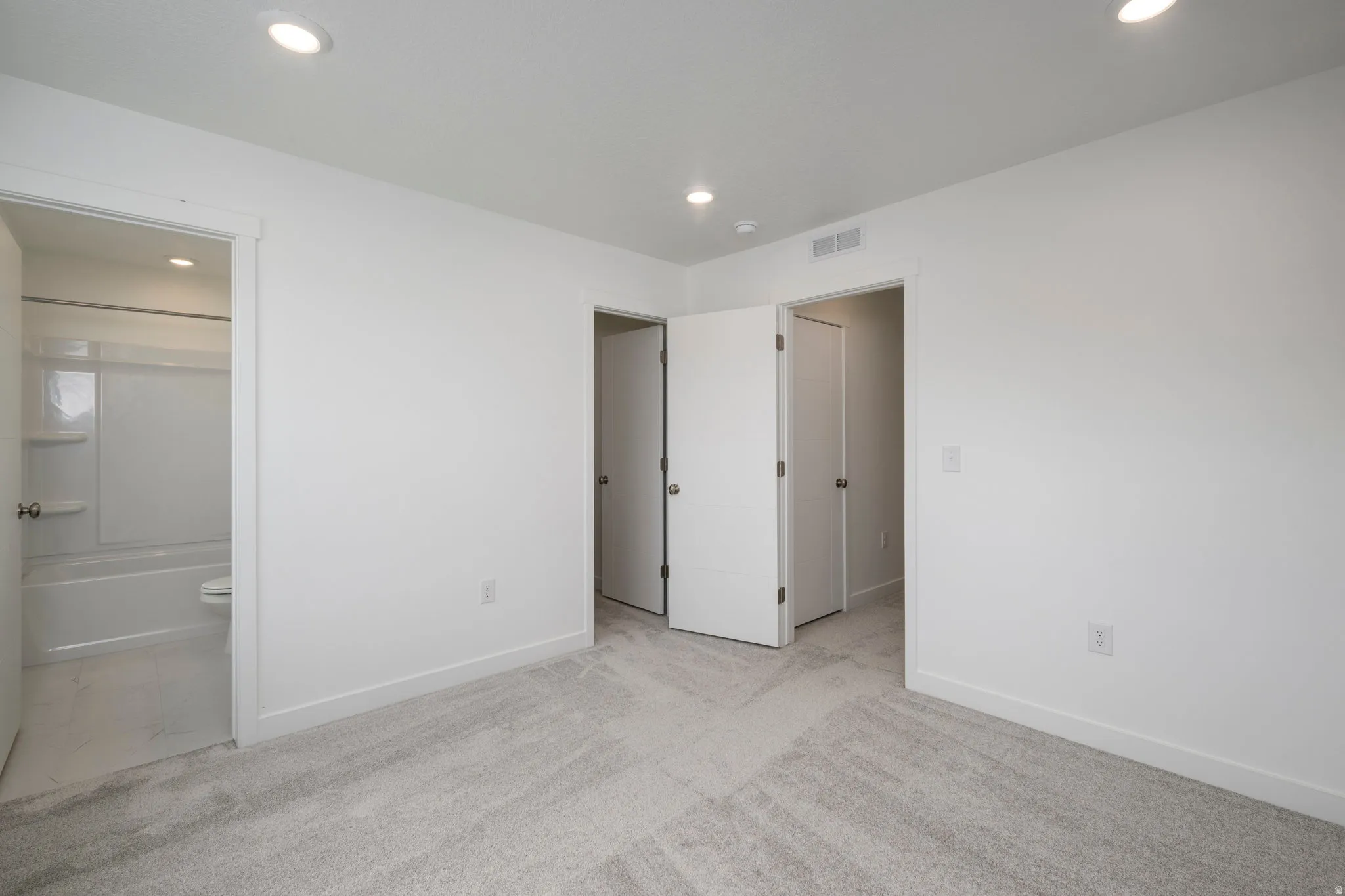 Unfurnished bedroom with light colored carpet, ensuite bathroom, and recessed lighting