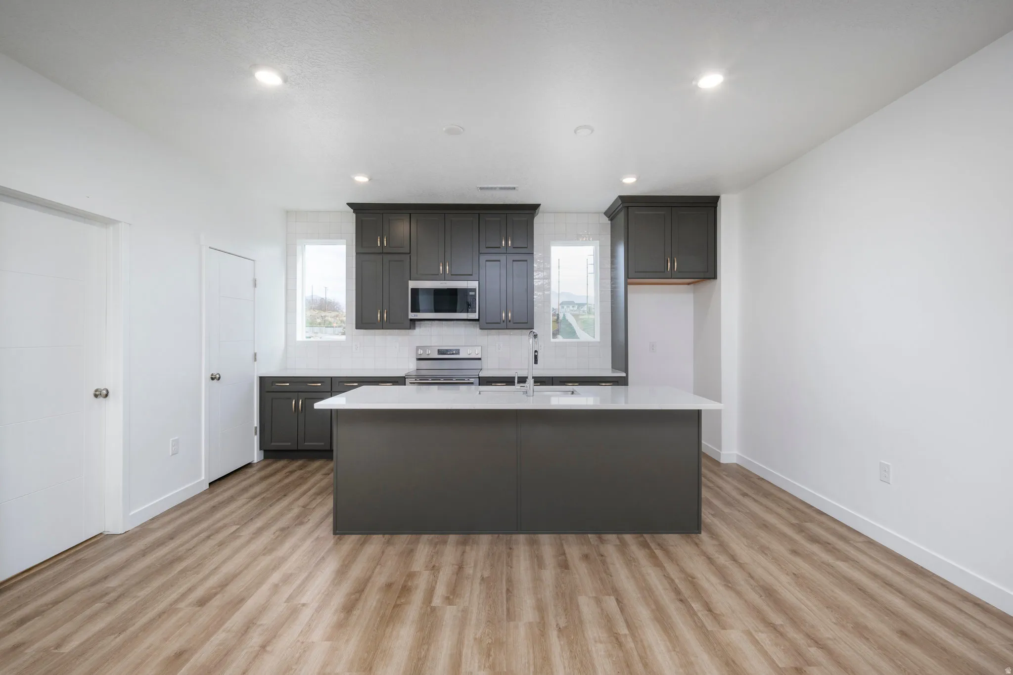 Kitchen with a kitchen island with sink, appliances with stainless steel finishes, plenty of natural light, tasteful backsplash, and recessed lighting