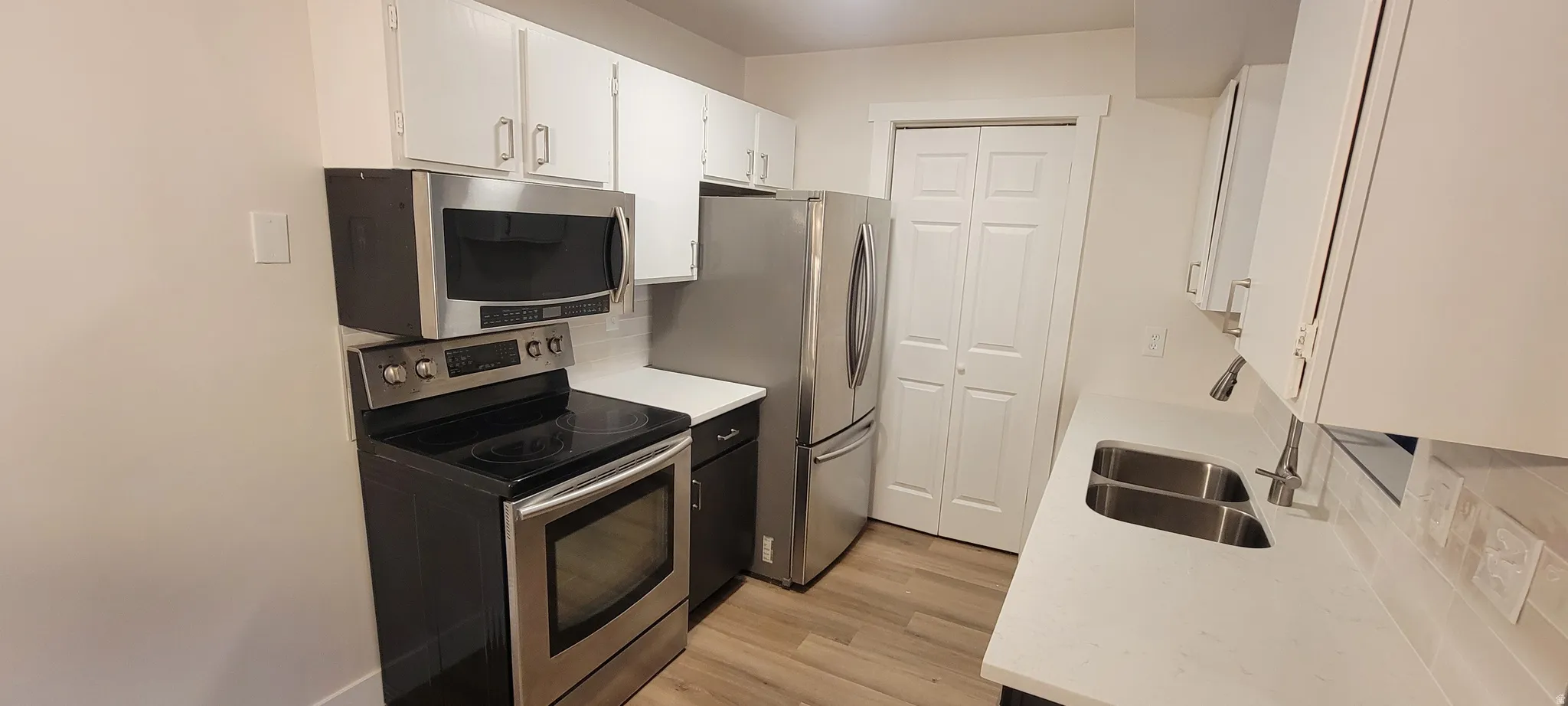 Kitchen with appliances with stainless steel finishes, decorative backsplash, white cabinetry, and light wood finished floors