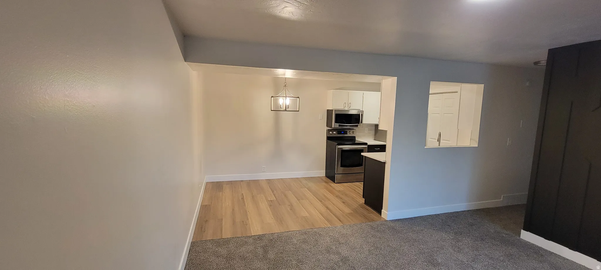Kitchen featuring light countertops, appliances with stainless steel finishes, white cabinetry, light carpet, and decorative light fixtures