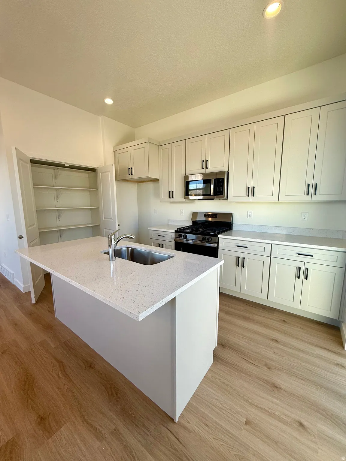 Kitchen with recessed lighting, stainless steel appliances, light stone countertops, a kitchen island with sink, and light wood-type flooring