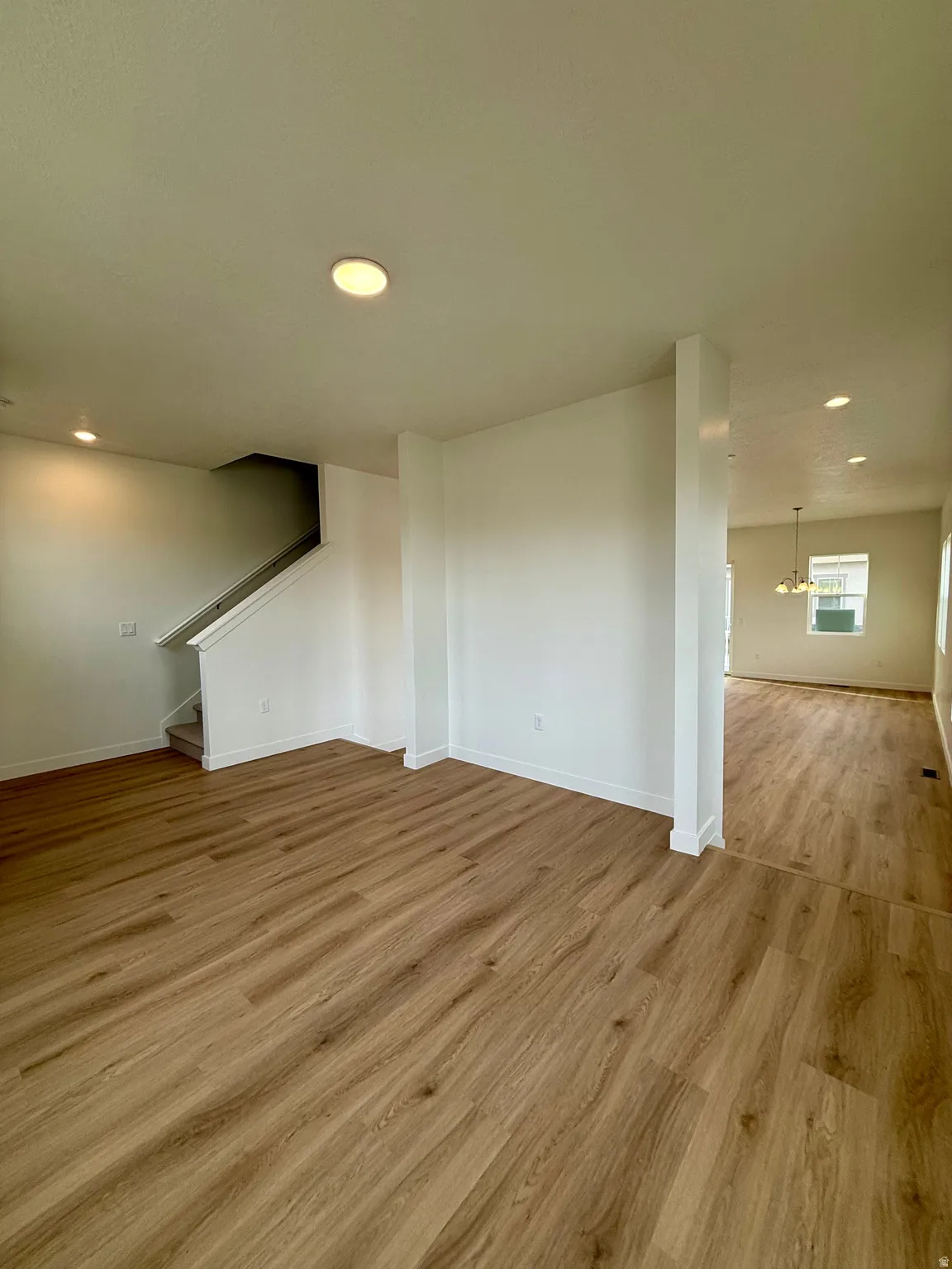 Unfurnished living room featuring recessed lighting, a chandelier, light wood-style floors, and stairs