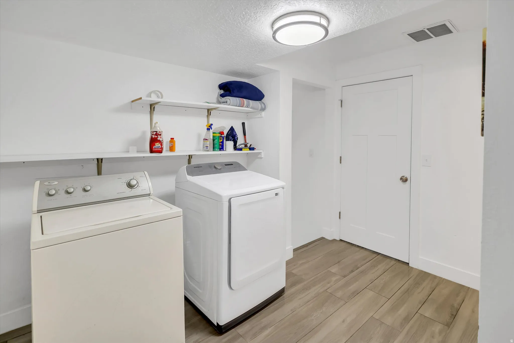 Laundry room with independent washer and dryer, a textured ceiling, and light wood-style flooring