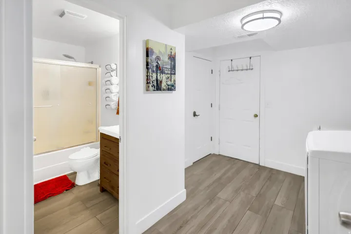 Full bathroom featuring vanity, light wood finished floors, shower / bath combination with glass door, a textured ceiling, and washer / dryer