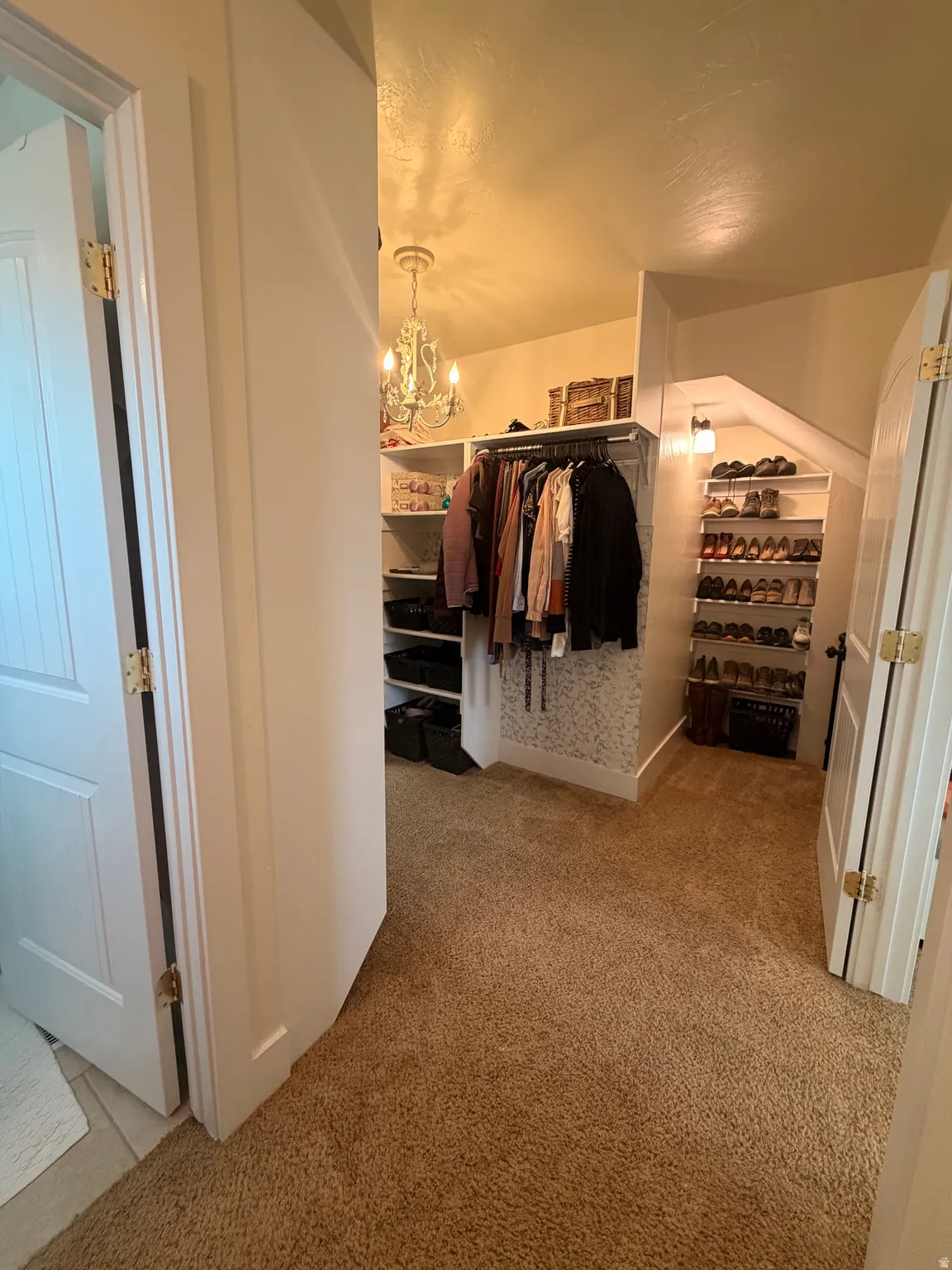 Walk in closet with a chandelier and light colored carpet