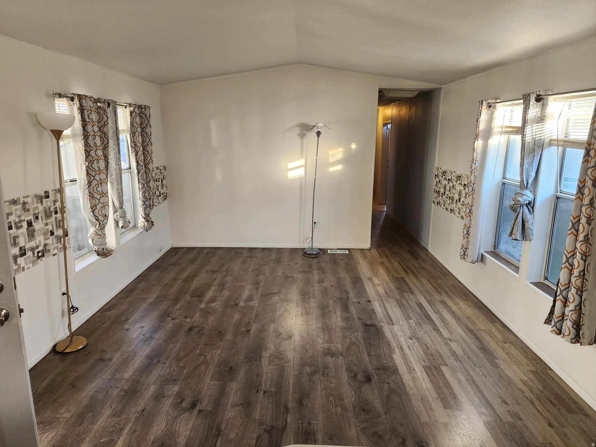 Empty room with dark wood-type flooring, vaulted ceiling, and plenty of natural light