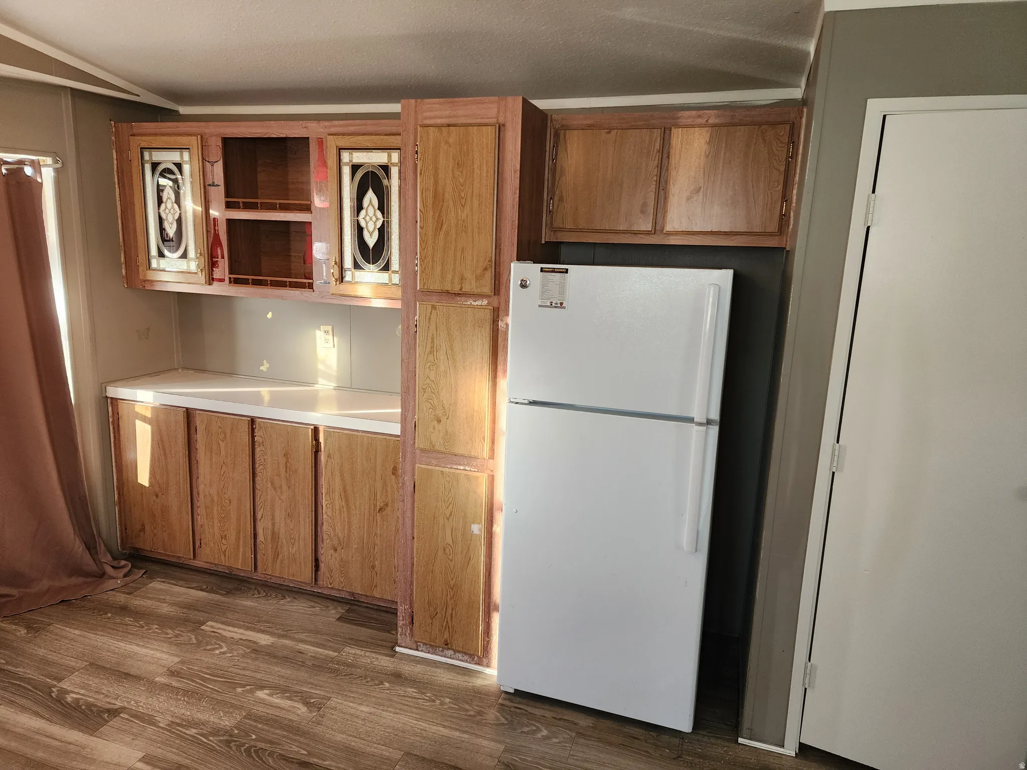 Kitchen with freestanding refrigerator, open shelves, light countertops, dark wood-style floors, and brown cabinets