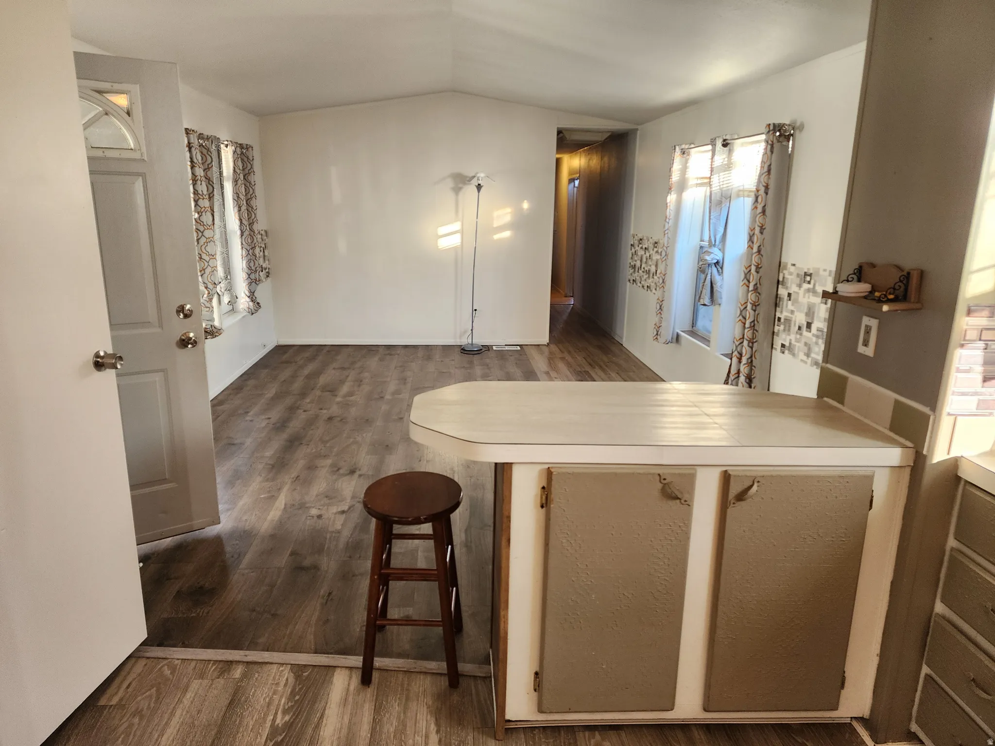 Kitchen featuring a peninsula, dark wood-type flooring, vaulted ceiling, light countertops, and a kitchen breakfast bar