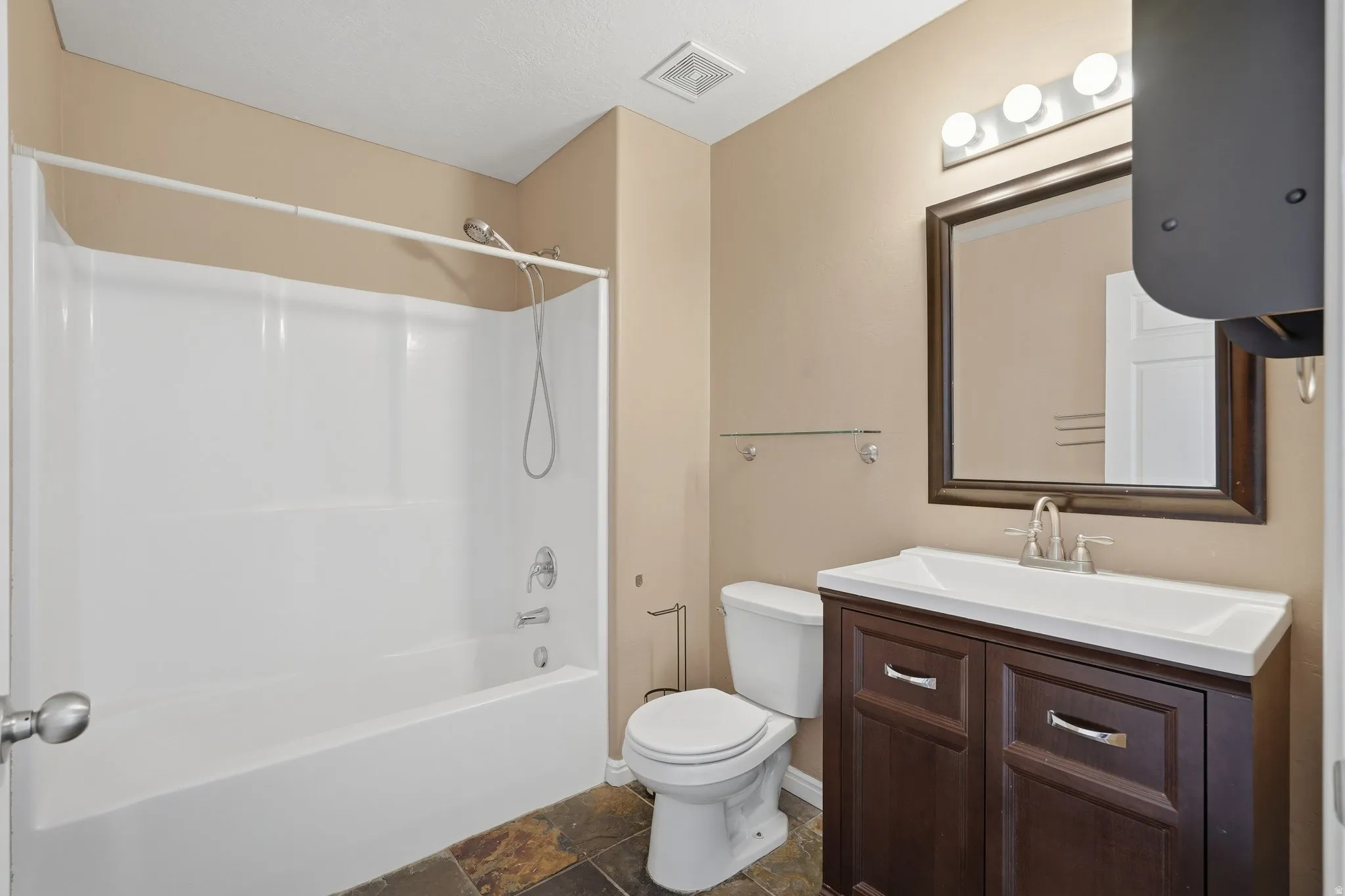 Full bath with vanity, shower / washtub combination, and dark stone finish floors