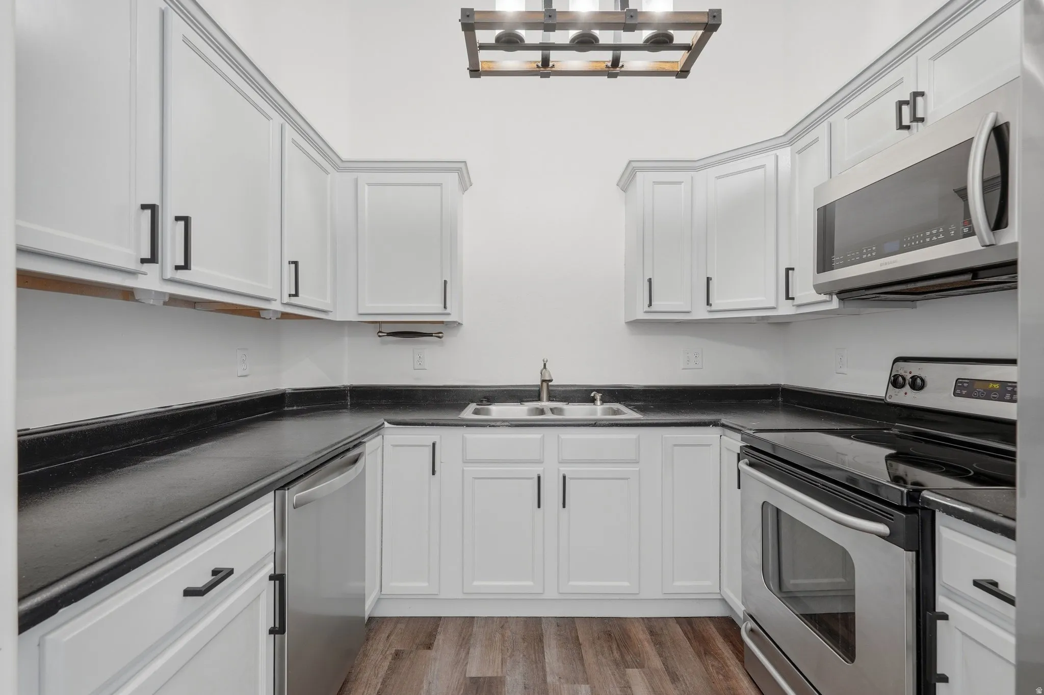 Kitchen featuring stainless steel appliances, dark countertops, light wood-style flooring, and white cabinetry