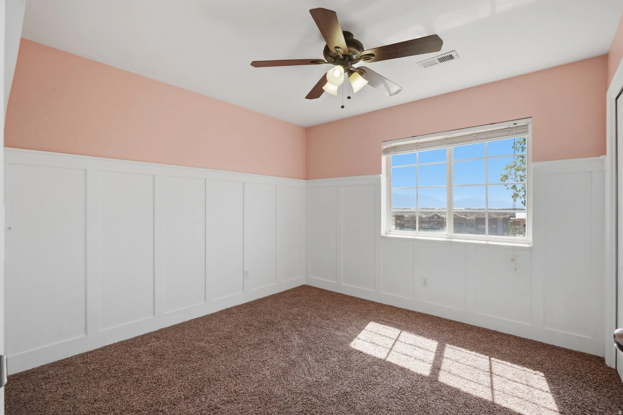 Spare room featuring a decorative wall, a wainscoted wall, ceiling fan, and dark colored carpet