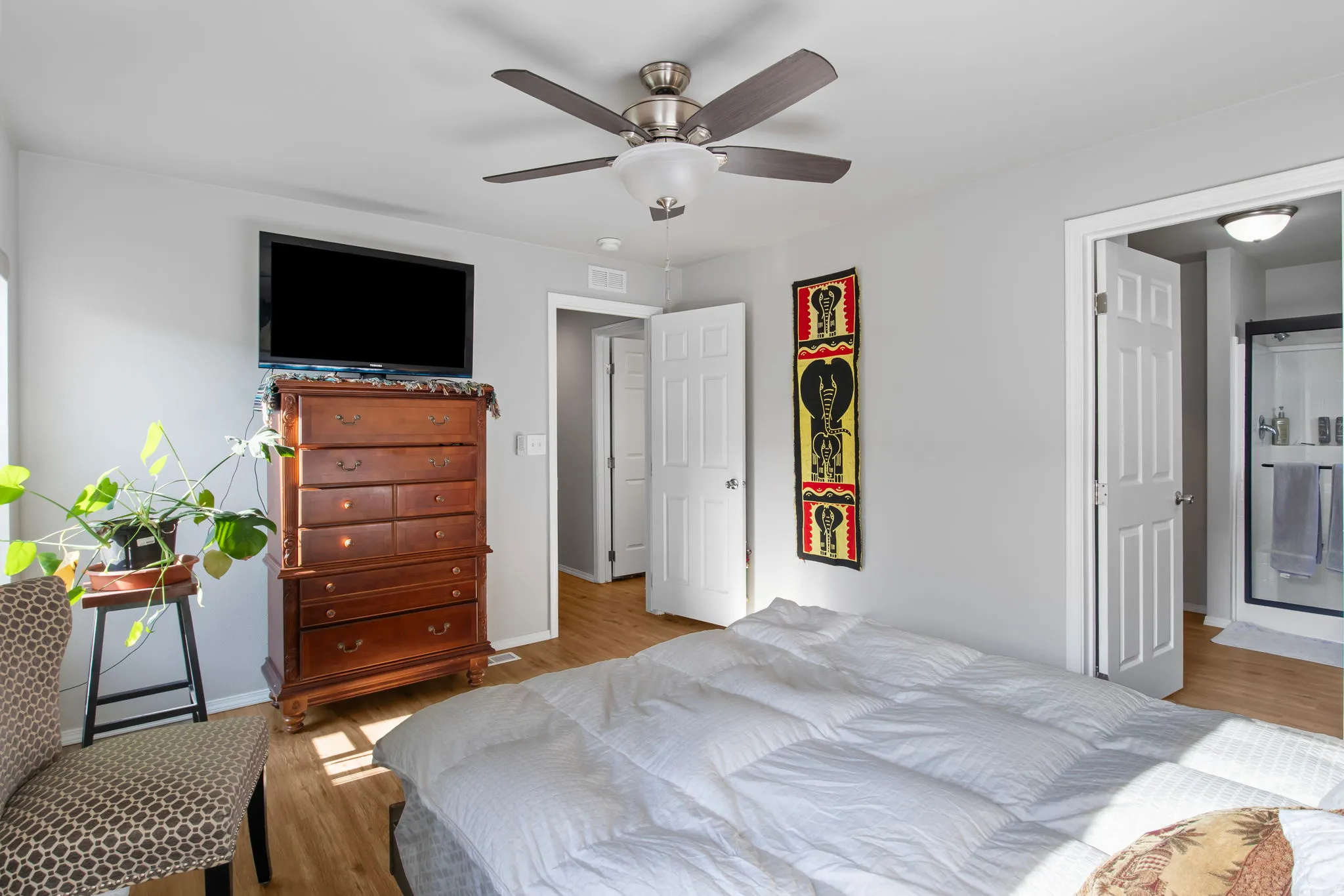 Bedroom with light wood finished floors, ceiling fan, and ensuite bathroom