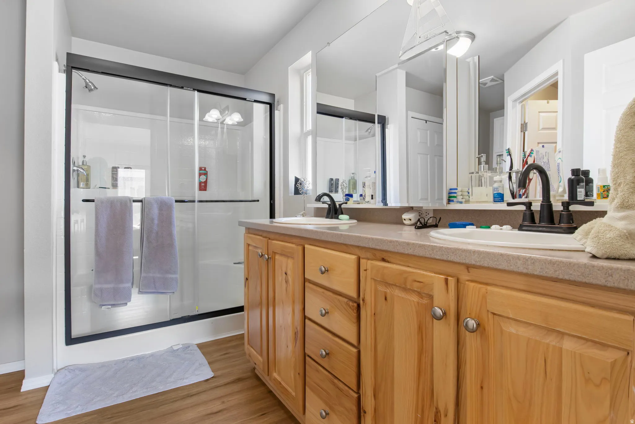 Bathroom with double vanity, light wood finished floors, and a shower stall