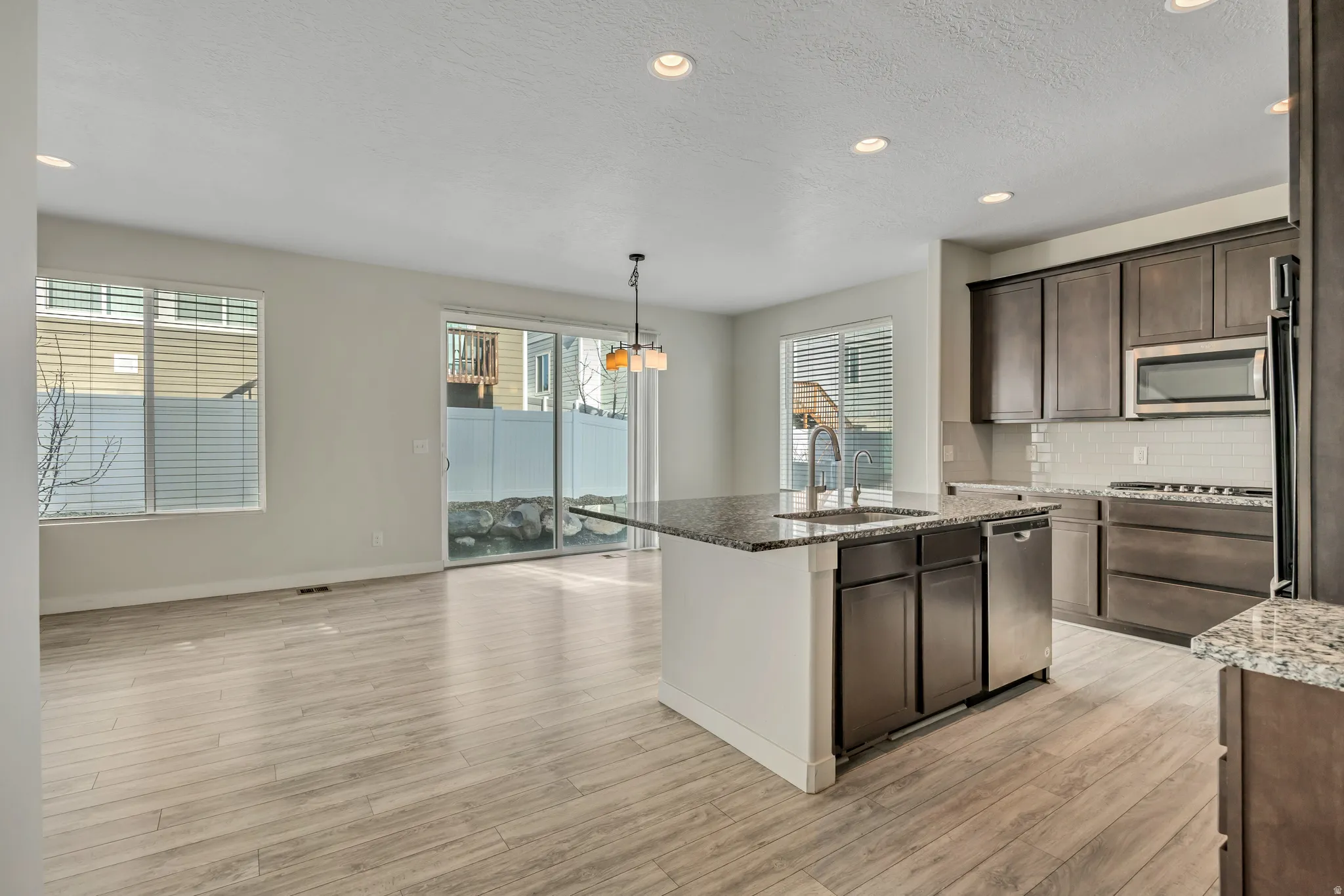 Kitchen with dark stone countertops, recessed lighting, a kitchen island with sink, dark brown cabinetry, and hanging light fixtures