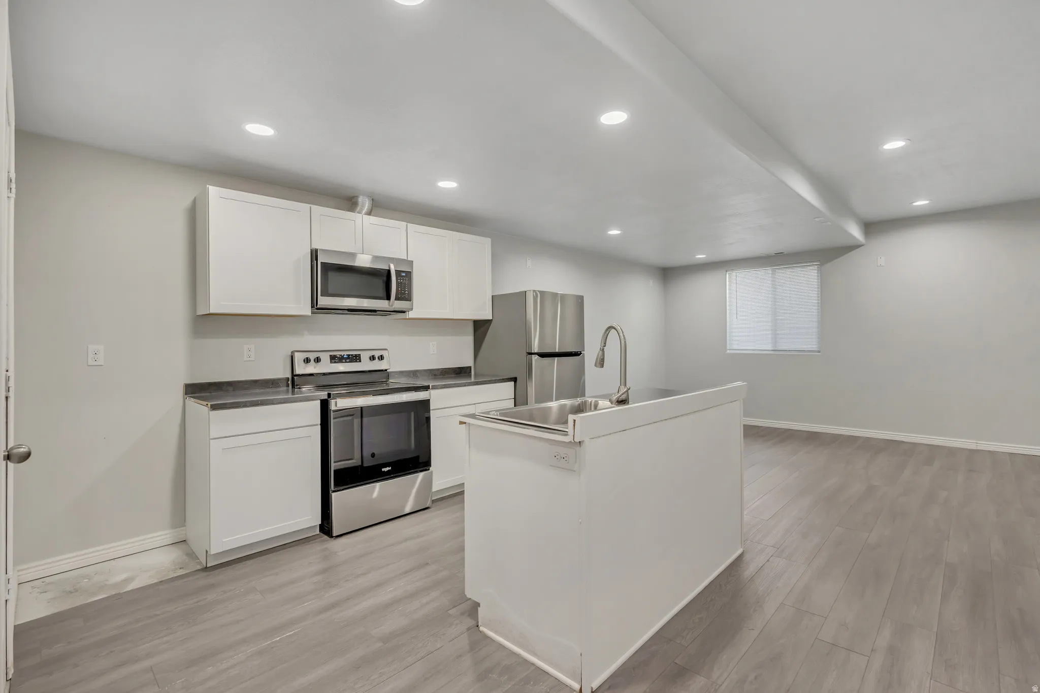 Kitchen with stainless steel appliances, white cabinetry, light wood-style flooring, recessed lighting, and an island with sink
