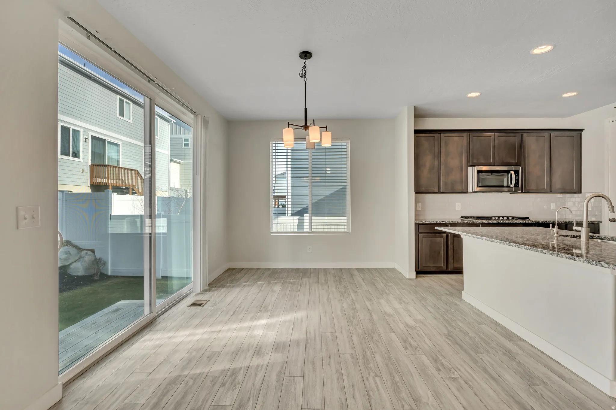 Kitchen with dark brown cabinets, light stone countertops, decorative light fixtures, light wood-style flooring, and backsplash