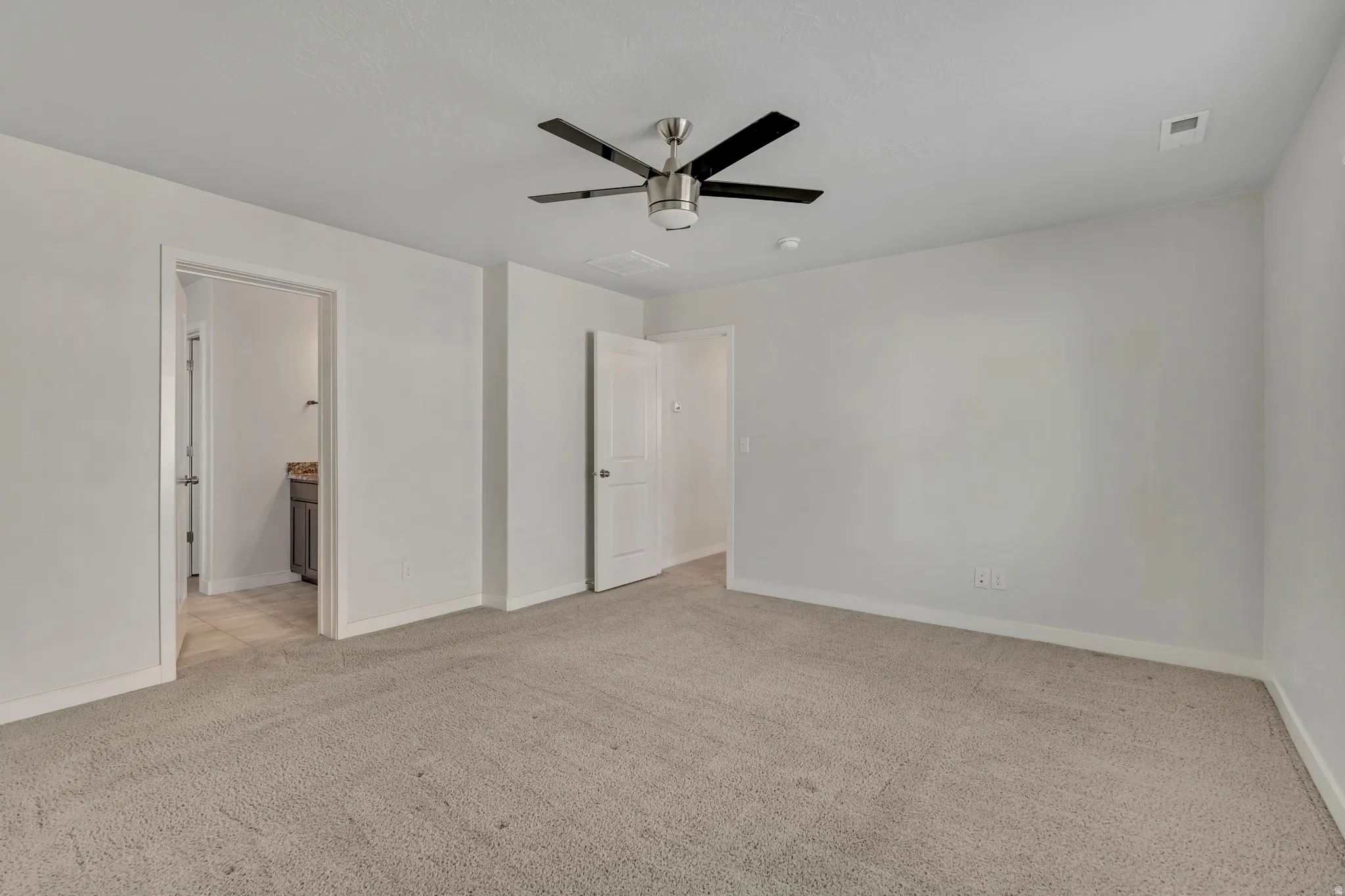 Unfurnished bedroom featuring light colored carpet, a ceiling fan, and ensuite bath