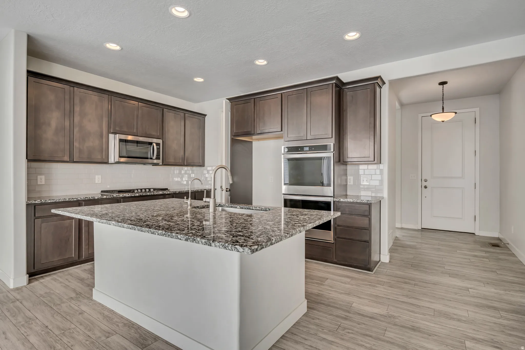 Kitchen with appliances with stainless steel finishes, dark stone countertops, dark brown cabinetry, tasteful backsplash, and recessed lighting