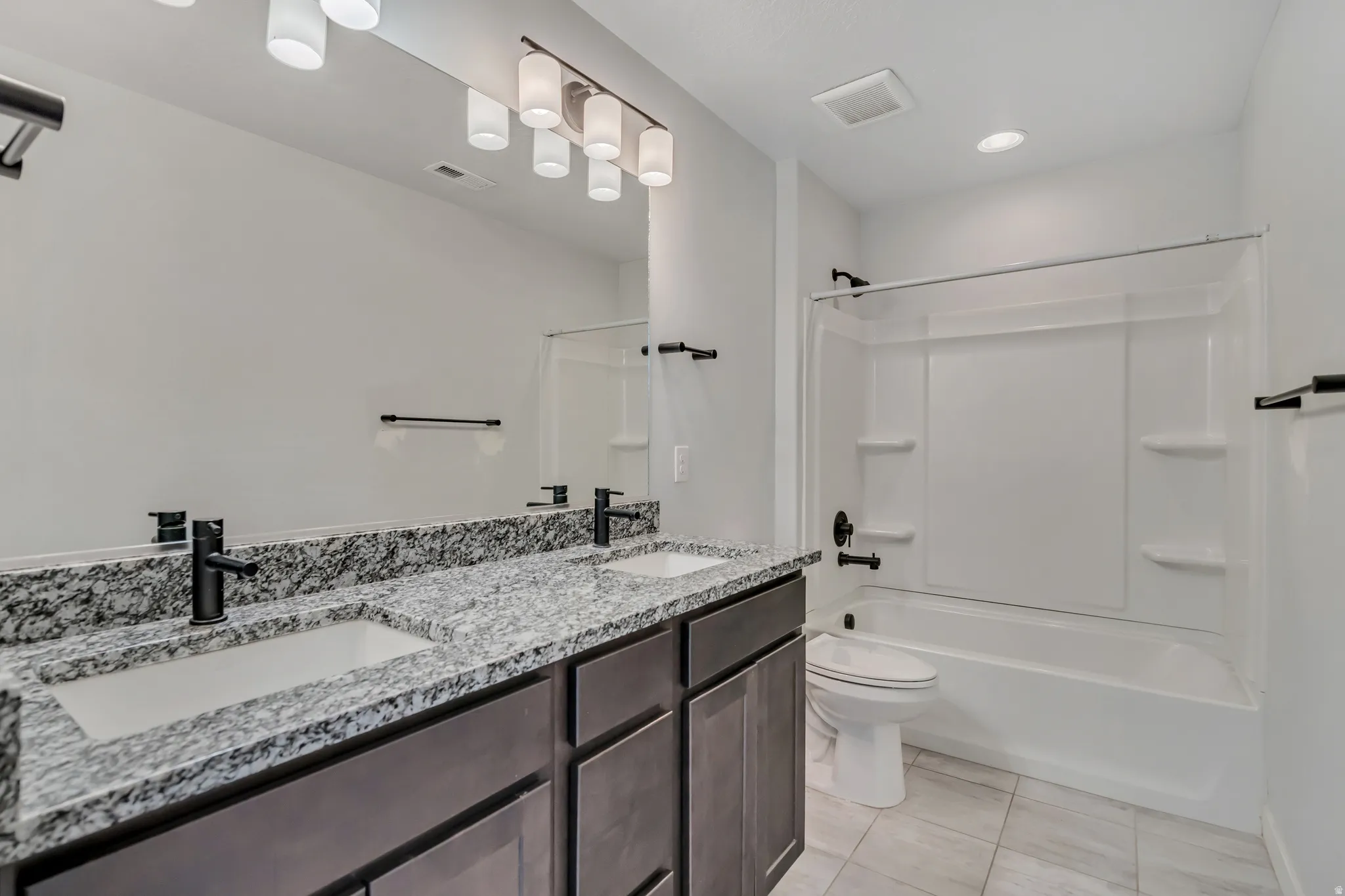 Bathroom with double vanity, shower / washtub combination, and light tile patterned floors