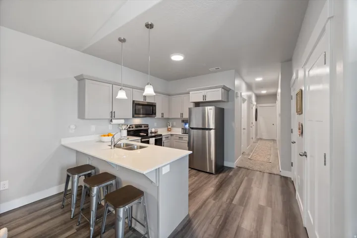 Kitchen featuring stainless steel appliances, decorative light fixtures, a breakfast bar, a peninsula, and dark wood-style flooring