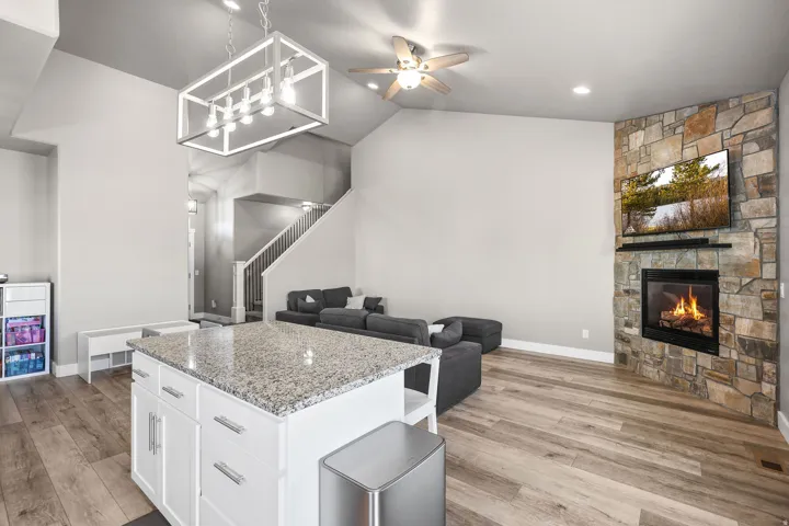 Kitchen with light stone countertops, open floor plan, white cabinets, light wood-type flooring, and lofted ceiling
