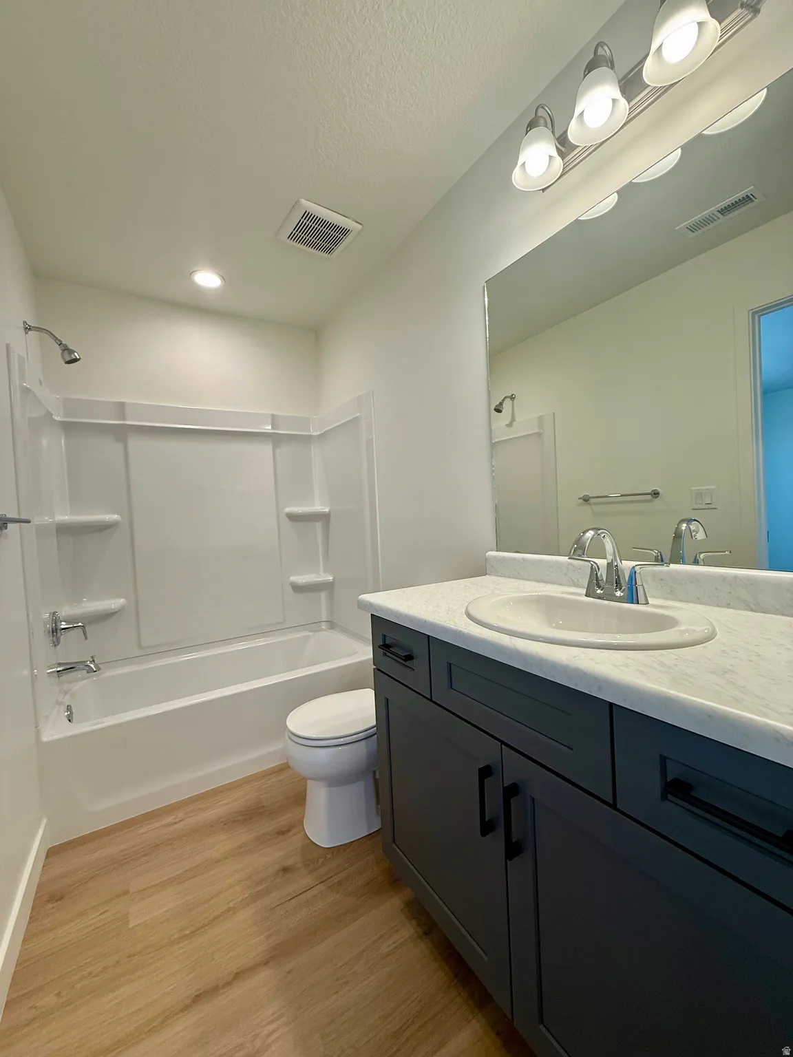 Bathroom featuring shower / tub combination, vanity, light wood-style floors, and a textured ceiling
