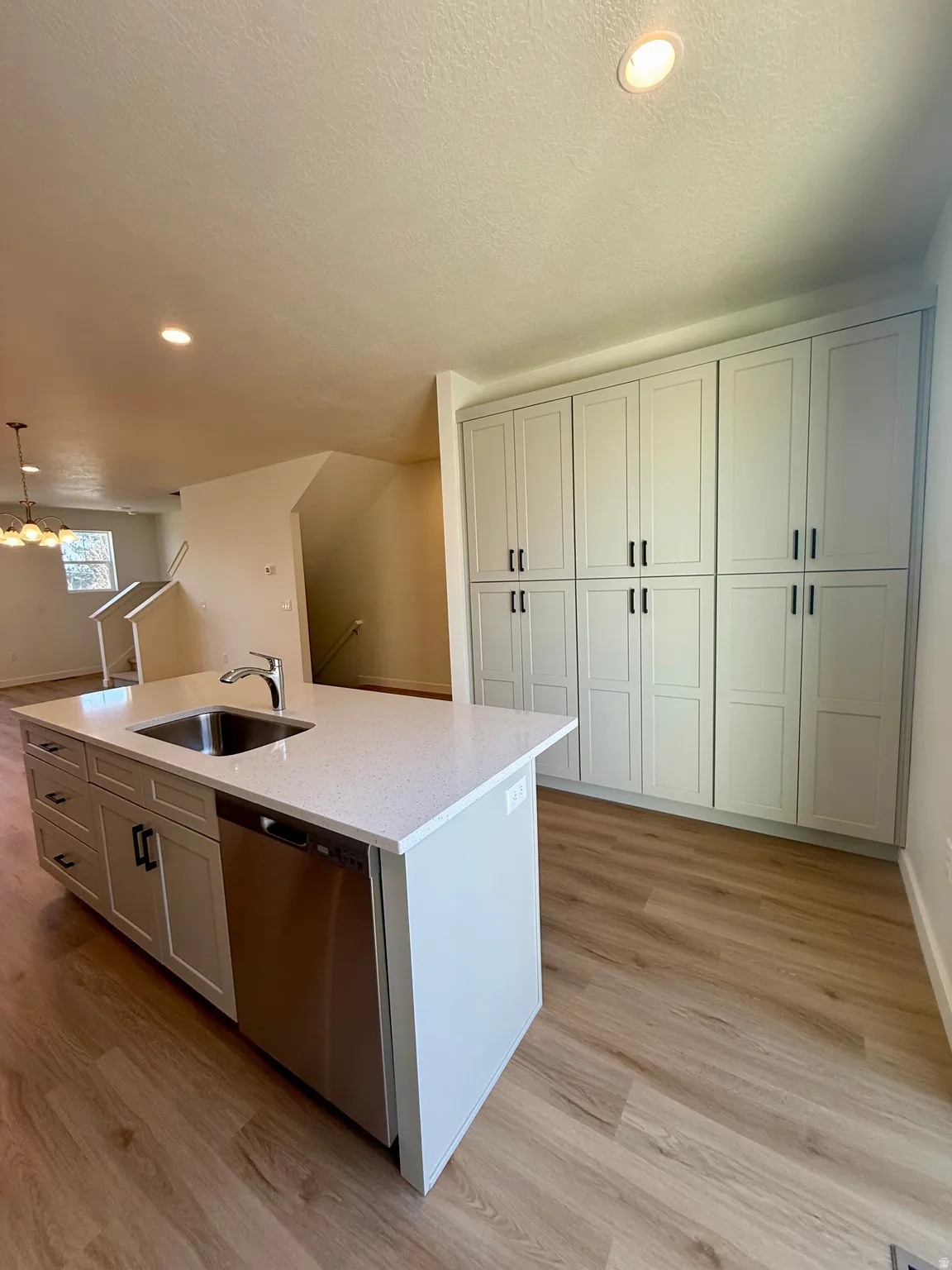 Kitchen with stainless steel dishwasher, an island with sink, light stone countertops, light wood-style flooring, and recessed lighting