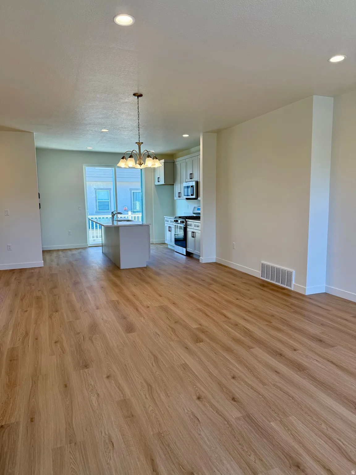 Unfurnished living room featuring a chandelier, light wood-style flooring, recessed lighting, and a textured ceiling