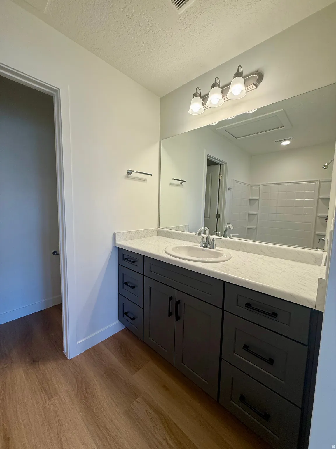 Bathroom with vanity, a textured ceiling, light wood finished floors, and a shower