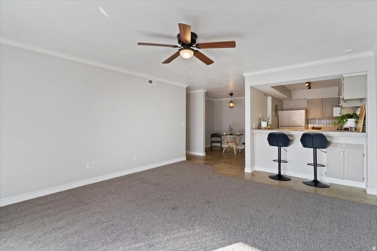 Unfurnished living room with crown molding, light colored carpet, and ceiling fan