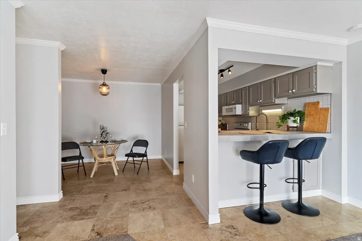 Kitchen featuring a kitchen breakfast bar, light countertops, ornamental molding, white microwave, and backsplash