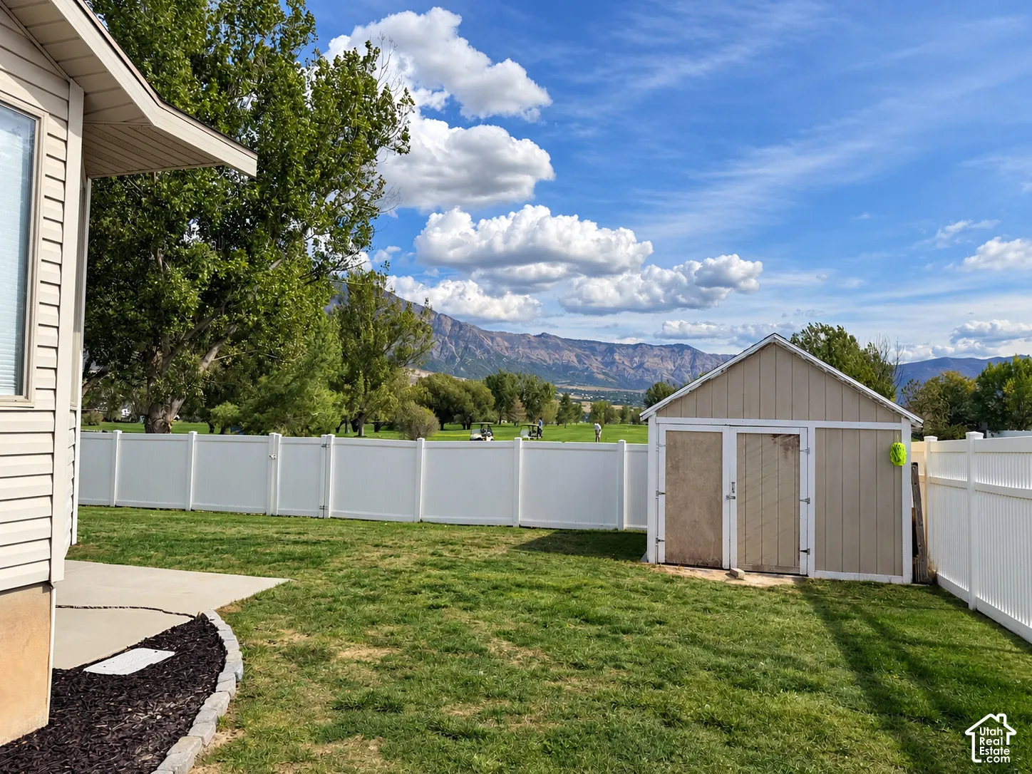 Expansive lawn with a white privacy fence, concrete patio, and a storage shed