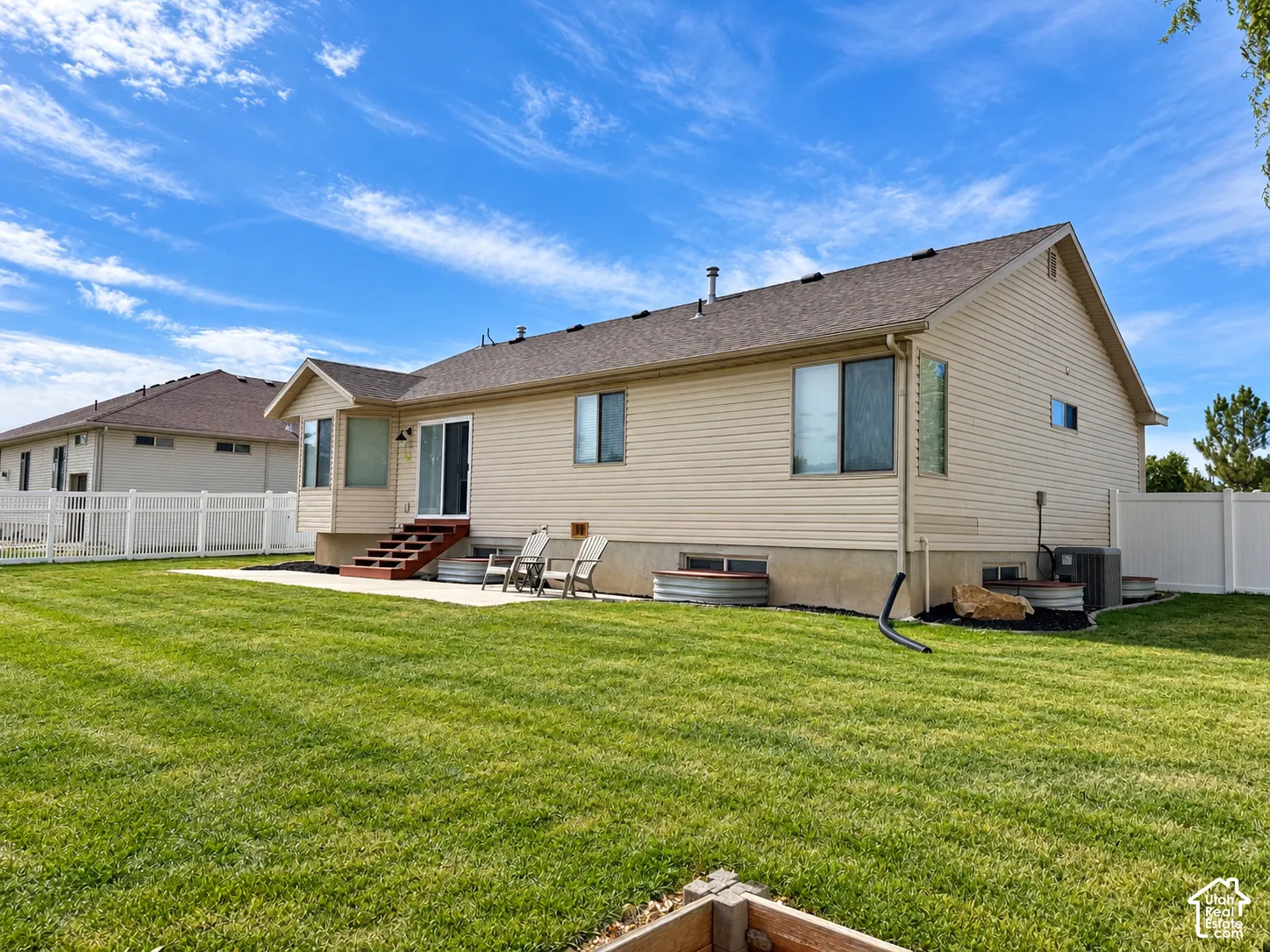 Expansive backyard with a manicured lawn, concrete patio, and a white vinyl fence