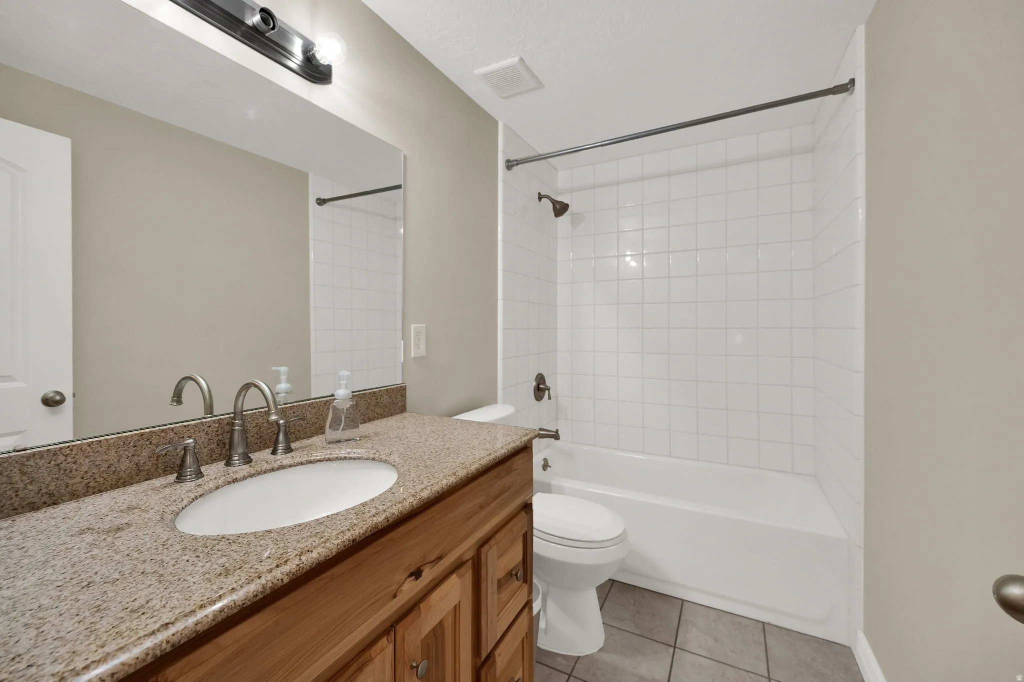 Bathroom featuring washtub / shower combination, vanity, and light tile patterned flooring