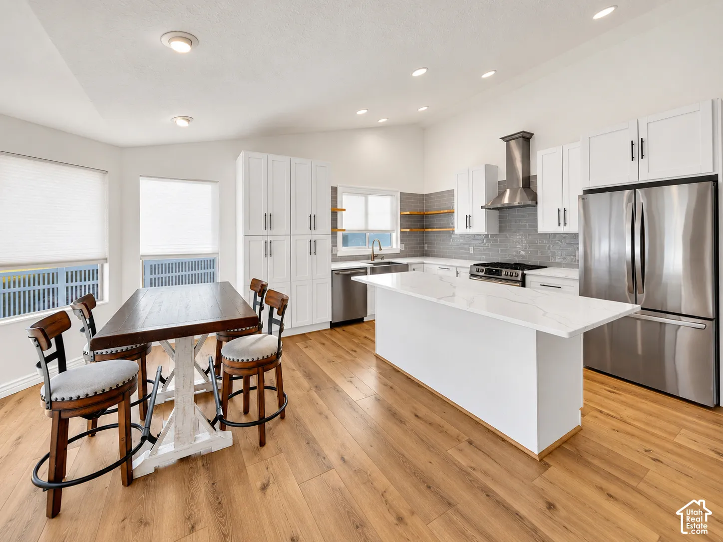 Modern kitchen featuring wood-finish flooring, white cabinetry, stainless steel appliances, a center island with a light-toned countertop, and a tile backsplash