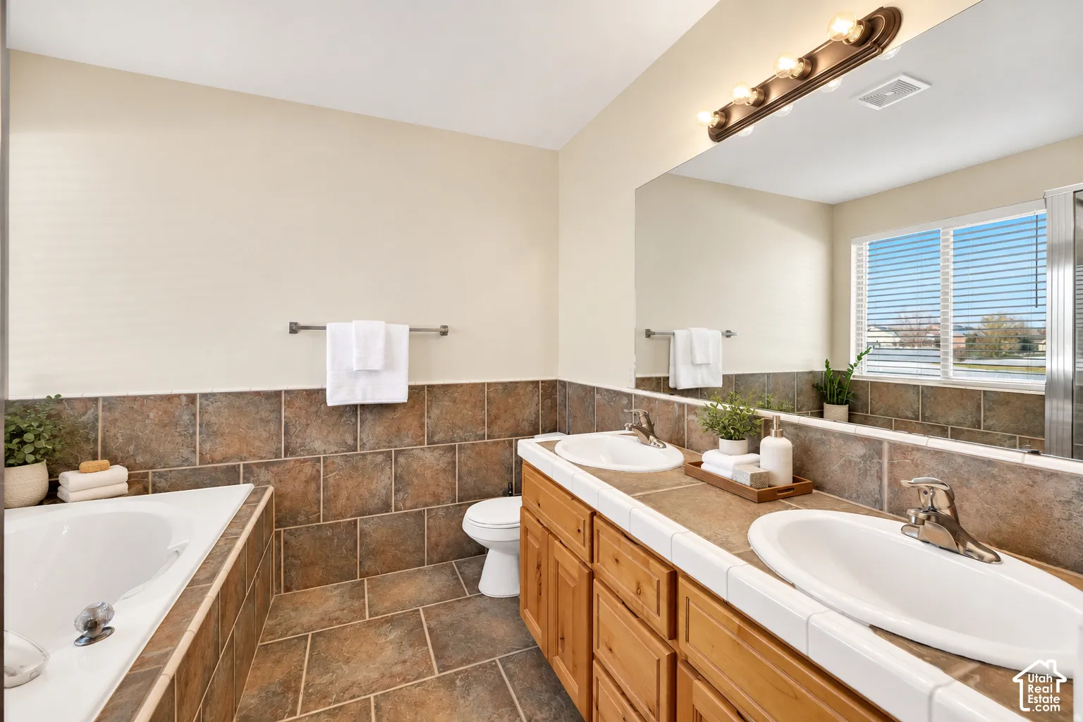 Dual vanity with wood-finish cabinetry, tile countertop, and integrated sinks