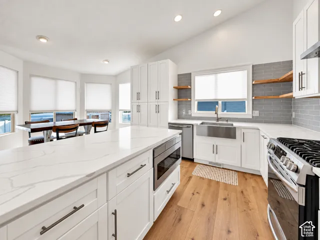 Kitchen featuring white cabinetry, wood-finish flooring, a farmhouse-style sink, and a tiled backsplash