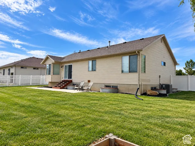 Expansive backyard with a manicured lawn, concrete patio, and a white vinyl fence