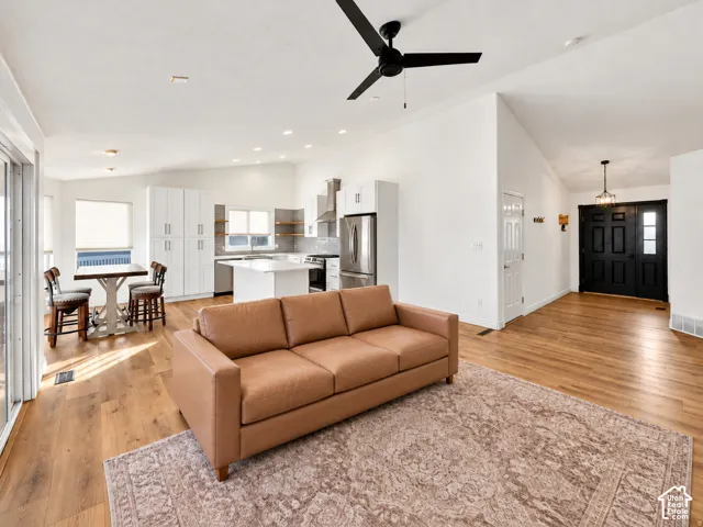 Vaulted ceilings, wood-finish flooring, white cabinetry, stainless steel appliances, and a black paneled entry door