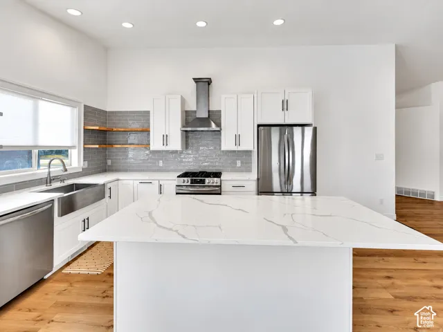 Kitchen featuring a large central island with a light-toned countertop, white cabinetry with dark hardware, stainless steel appliances, and wood-finish flooring