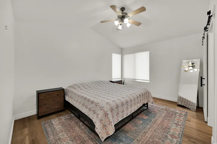 Bedroom featuring a barn door, vaulted ceiling, a ceiling fan, and wood finished floors
